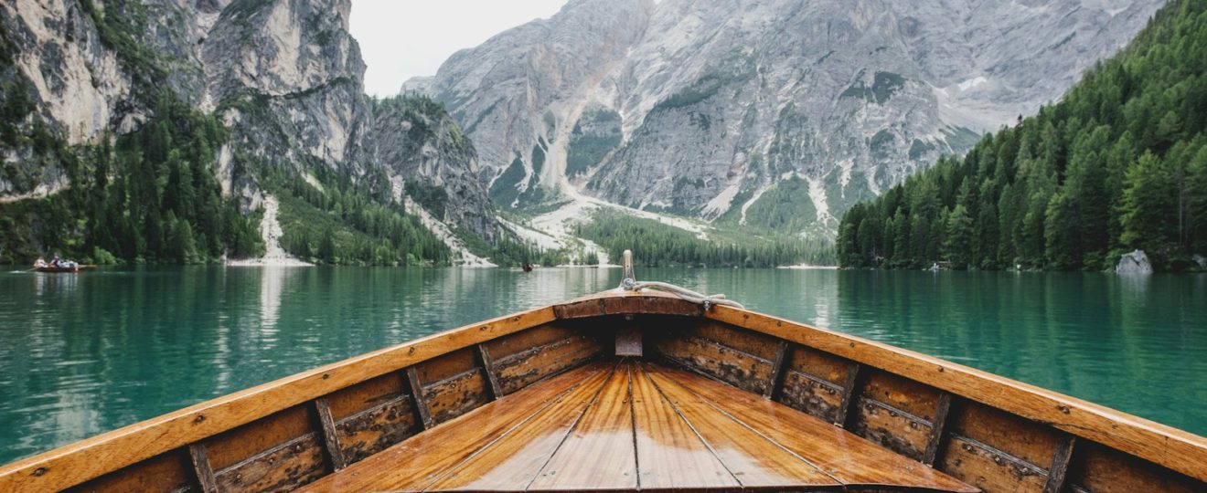 brown wooden boat moving towards the mountain